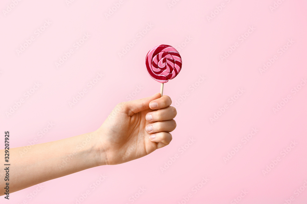 Female hand with sweet lollipop on color background