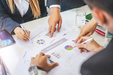 businesswoman and businessman working together in a group in an office, all pointing on the paper together in teamwork conversing and planning strategy using data and statistics of charts and graphs