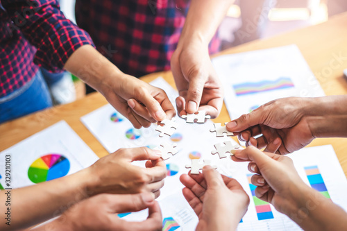 Fotomural employees standing around in a circle holding jigsaw pieces each matching it against one another, representing teamwork problem solving, help and support within small businesses or company