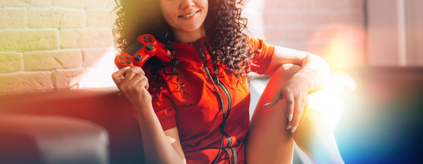 young girl plays video games on a red joystick sitting on the couch, happy smiling face, modern lights.