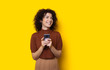 © Strelciuc - Stunning curly haired caucasian girl is smiling on a yellow wall while texting with somebody
