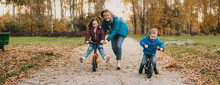 Smiling Caucasian Mother Is Playing With Her Small Kids While Teaching Them To Ride The Bike