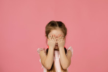 Cute Little Child Girl Closes Her Eyes With Her Hand On Pink Background. I See Nothing