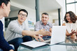 © DragonImages - Smiling young Asian entrepreneur pointing at laptop screen when discussing figures in financial report with colleagues at meeting