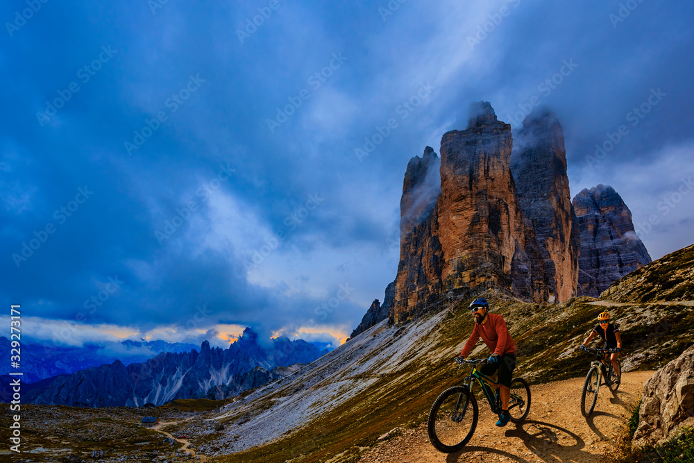 Cycling outdoor adventure in Dolomites. Cycling woman and man  on electric mountain bikes in Dolomites landscape. Couple cycling MTB enduro trail track. Outdoor sport activity. - obrazy, fototapety, plakaty 