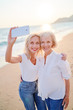 © luengo_ua - Outdoor portrait of smiling happy caucasian senior mother with her adult daughter taking selfie on smartphone on sea beach.