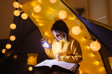 Wall Mural - young female child reading encyclopedia in a home made livingroom tent with light balls.