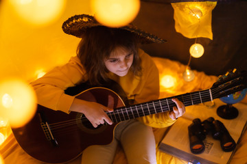 Wall Mural - little girl playing acoustic guitar under the tent in a living room.