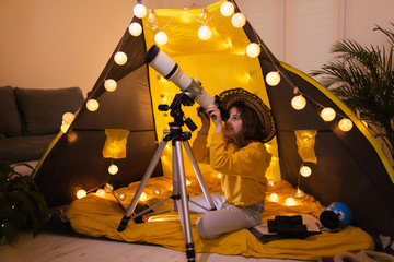 Wall Mural - small girl using telescope at home living room in a tent.