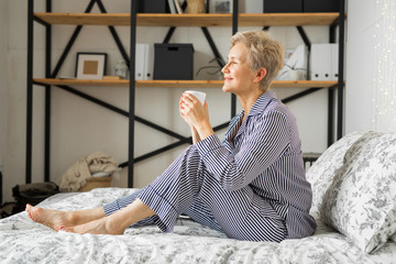 adult elderly woman in pajamas in bed in the bedroom with a mug