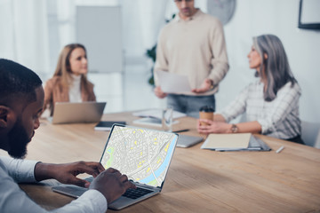 Wall Mural - selective focus of african american man using laptop with map website and his colleagues talking on background