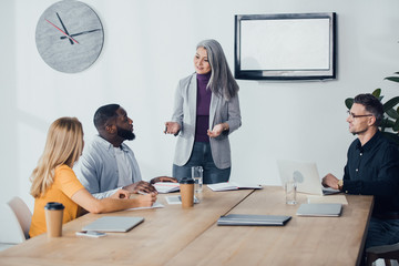 smiling asian businesswoman talking with multicultural colleagues in office