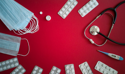 Wall Mural - Medical masks,pills in blister packs,homeopathic remedies,stethoscope and thermometer lying on bright red background around copy space in center.Concept of prevention,diagnosis and treatment of virus