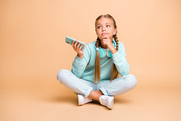 Wall Mural - Full body photo of beautiful little lady listen earphones song sit floor legs crossed boring lesson school waiting go home wear blue sweater jeans footwear isolated beige color background