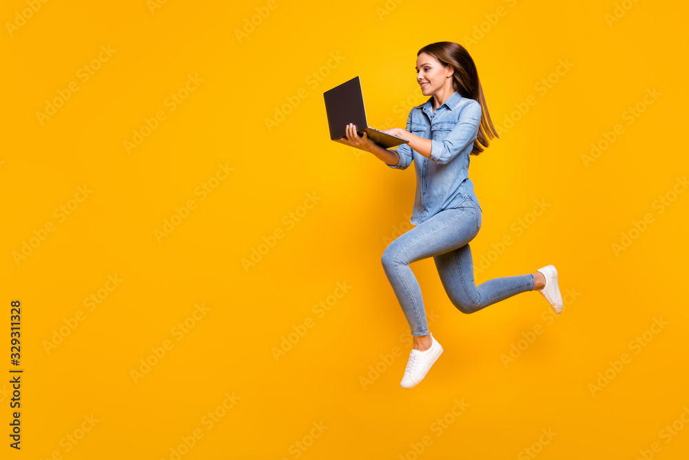 Full size profile photo of beautiful business lady jump high hold notebook hands hurry work browsing laptop wear casual denim outfit white sneakers isolated yellow color background - obrazy, fototapety, plakaty 