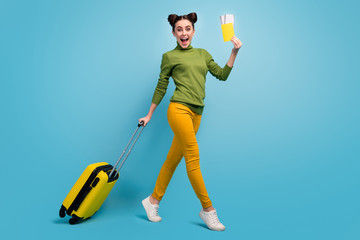 Poster - Full length profile photo of funny pretty lady hold tickets passport cheap flight rolling suitcase walk airport wear green turtleneck yellow pants footwear isolated blue color background