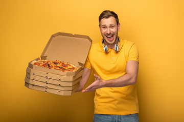 Wall Mural - happy man with headphones in yellow outfit holding pizza on yellow background