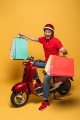 Wall Mural - happy delivery man in red uniform with shopping bags on scooter on yellow background