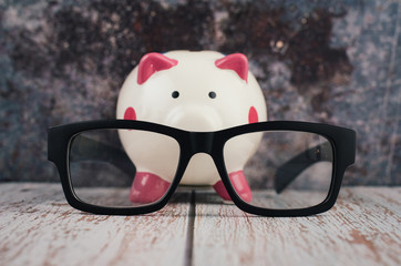 black frame eye glasses and piggybank on wooden desk