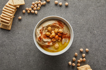 Wall Mural - Top view of bowl with delicious hummus, chickpea and crackers on grey background