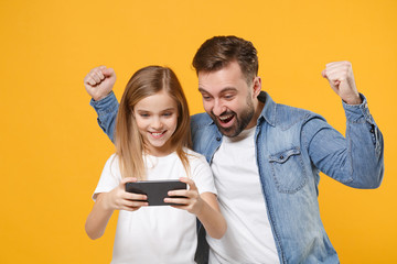 Wall Mural - Joyful bearded man with cute child baby girl. Father little kid daughter isolated on yellow background. Love family day parenthood childhood concept. Play game with mobile phone, doing winner gesture.