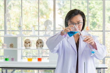 Poster - Discovering a cure for an Asian female scientist who is concentrated, holding a test tube and watching while working.