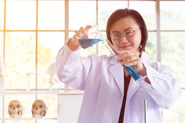 Poster - Discovering a cure for an Asian female scientist who is concentrated, holding a test tube and watching while working.