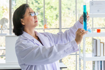 Poster - Discovering a cure for an Asian female scientist who is concentrated, holding a test tube and watching while working.