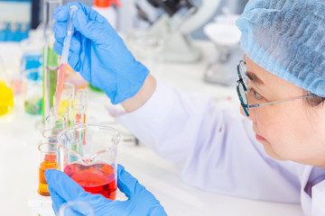 Poster - Discovering a cure for an Asian female scientist who is concentrated, holding a test tube and watching while working.