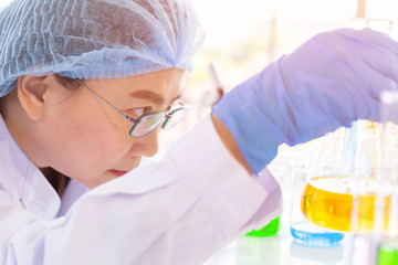 Poster - Discovering a cure for an Asian female scientist who is concentrated, holding a test tube and watching while working.