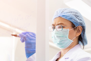 Poster - An Asian female scientist is writing down the formula for calculating chemistry on clear glass in a lab.