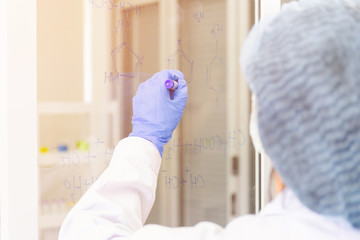 Poster - An Asian female scientist is writing down the formula for calculating chemistry on clear glass in a lab.