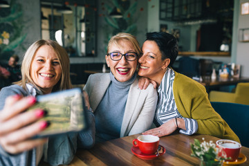 women friends on coffee break in cafe taking picture with mobile phone