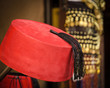 Colorful red fez in a Souk street bazaar stall in Medina, Marrakesh, Morrocco with golden out of focus jewelry in background