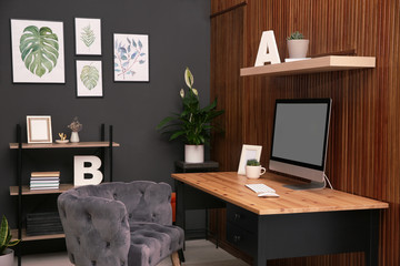 Poster - Comfortable workplace with computer near wooden wall in stylish room interior. Home office design