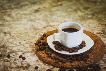 A small cup of espresso and coffee beans on a stand