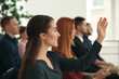 © New Africa - Young woman raising hand to ask question at business training indoors