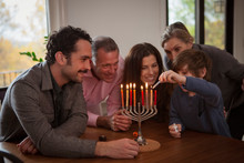 Happy Family Assisting Boy In Burning Candles On Menorah During Hanukkah Festival At Home