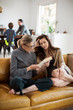 © Cavan for Adobe - Woman talking with mother reading book while sitting on sofa in living room