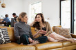 © Cavan for Adobe - Full length of woman listening to mother while sitting on sofa at home