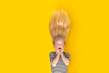 Surprised shocked little blonde girl with hair up over isolated yellow studio background. Emotion, expression. Copy space for text