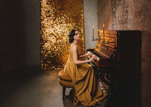 Young Woman With Finger Wave Hairstyle Gold Dress Vogue Fashion Old Style 1920 Play Piano Candles Romantic Burning. Retro Great Gatsby Backdrop Shine Sparkle Room Brick Wall. Musician Graduate Party