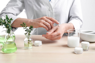 Woman applying natural cream onto hand in cosmetic laboratory, closeup