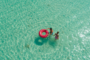 Wall Mural - .Summer holiday fashion concept - tanning couple at the beach on a turquoise sea shot from above. Top view from drone. Aerial view of slim woman and man sunbathing lying on a beach in Thailand.