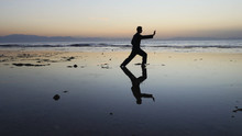 Silhouette Of Man Practiceing Qigong Exercises At Sunset By The Sea