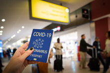Close Up Of Woman Holding A Passport With Coronavirus And COVID Words Over A Blurred Airport Background. Digital Composite Symbolizing The Global Spread Of The Coronavirus Through Global Air Traffic