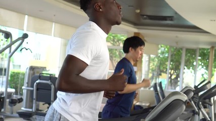 Wall Mural - Multiracial sportsmen working out on treadmills in gym on daytime. Multiethnic Asian and African American males running on treadmills.