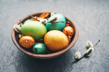 Wall Mural - Bright easter eggs in a clay bowl and fluffy willow branches on a dark background, soft focus. 