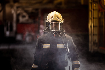 firefighter portrait wearing full equipment with oxigen mask. fire trucks in the background.