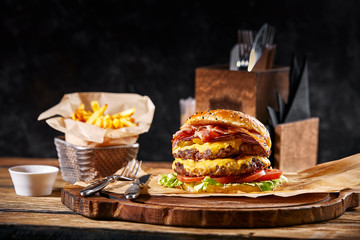 Fresh and juicy hamburger on a paper pillow with beer on a wooden table. Dark background, traditional american food. Junk food,...